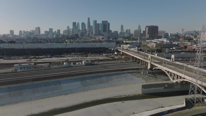 A city view of downtown Los Angeles shows cars moving along Fourth Street Bridge over the LA River around midday