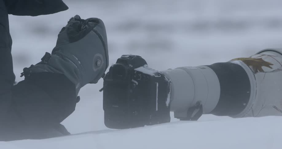 A person is lying near a large camera in the snow