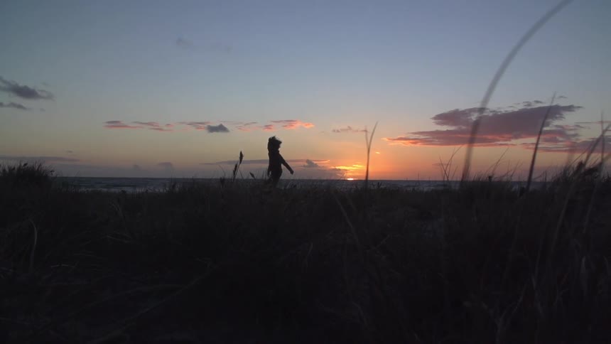 A young child runs on the beach at sunset