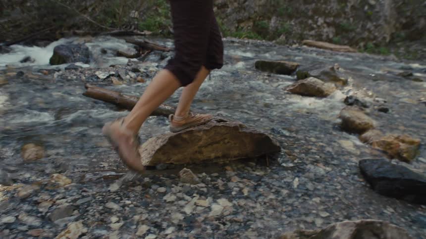Woman stepping on rocks while hiking across a flowing stream