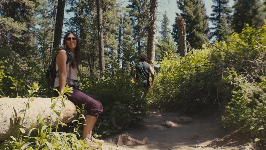 Man running on a trail and a woman sitting on a log in the forest