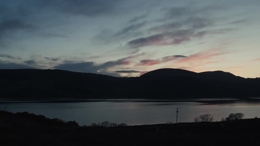 A calm lake reflects the fading light of dusk behind silhouetted hills and a colorful evening sky