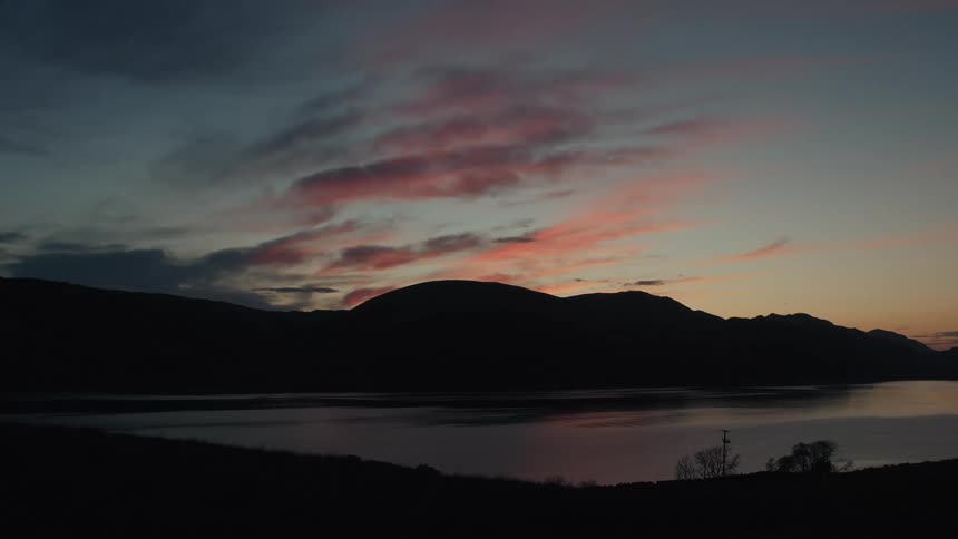 Silhouetted mountains and a calm lake under a colorful dusk sky