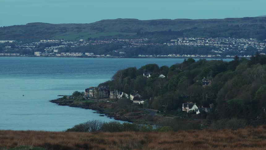 Coastal village by forest and water with hills and town across the bay