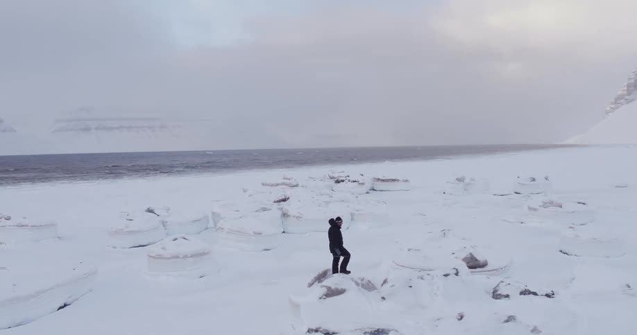 A man carrying a camera stands atop a snow covered rock