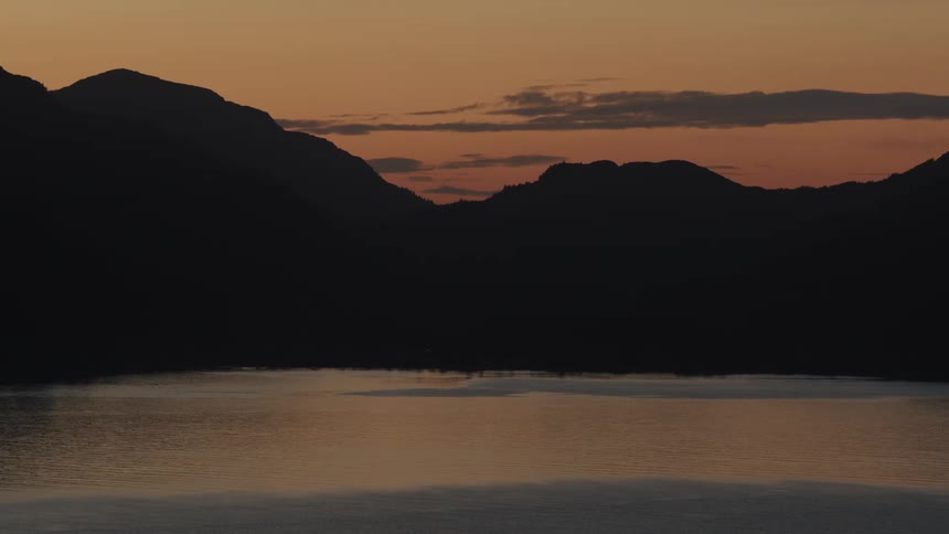 A still lake reflects silhouetted mountains at dusk
