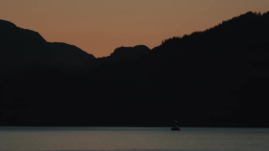 Silhouette of a boat in the sea surrounded by mountains at dawn