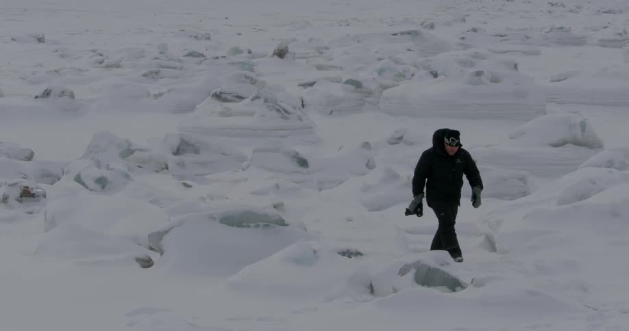 A man carrying a camera walks over icy and snowy terrain