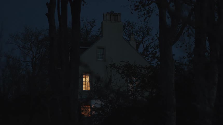 House with illuminated window at night in an environment surrounded by trees
