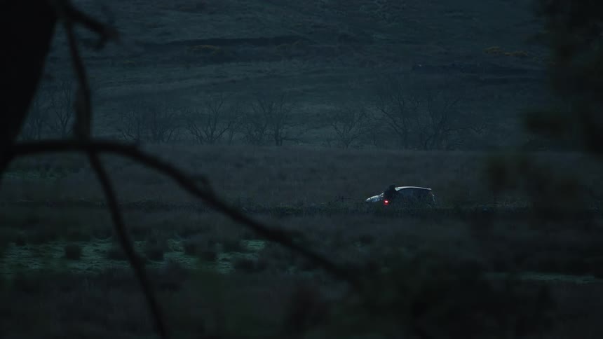 Car is parked on a deserted road at dusk with a person on a motorcycle approaching from the side