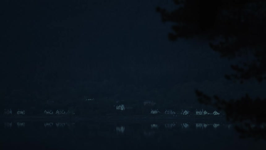 Dimly lit homes lining the shoreline of a lake cast reflections on the waters surface at night