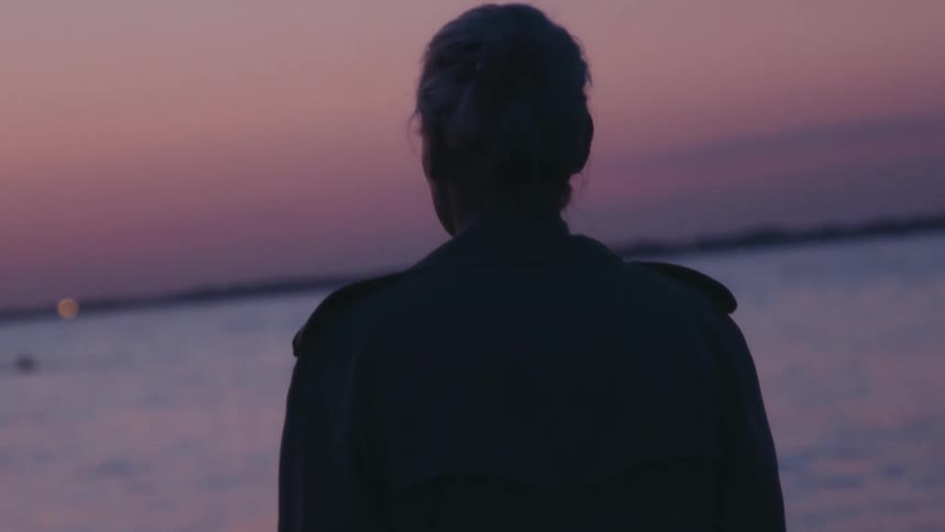 Silhouette of a woman from behind walking on the beach against a purple sky