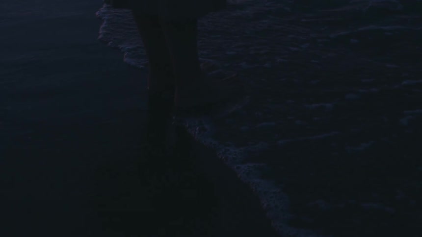 A woman is standing with her feet in the water at the beach
