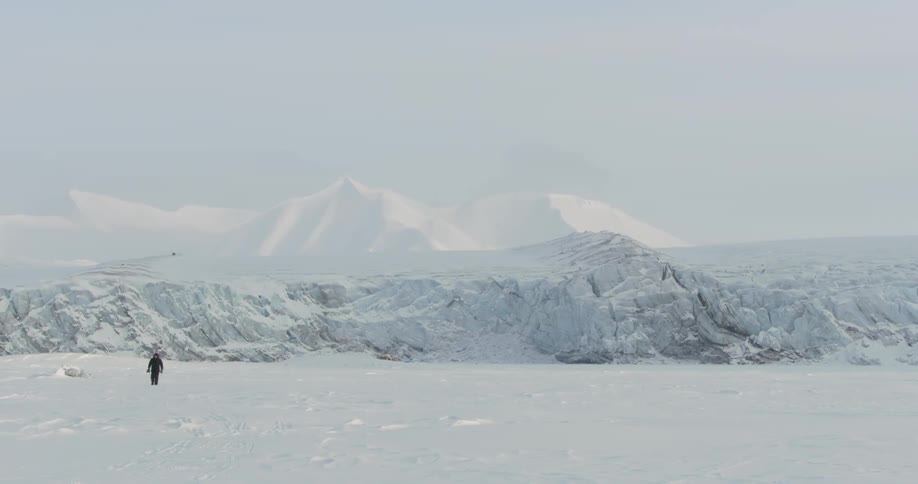 A man walking across a snow covered field with mountains in the background