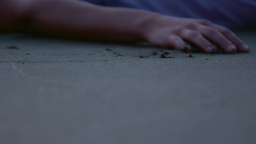 A person lies flat on the sand rubbing their right hand across the surface