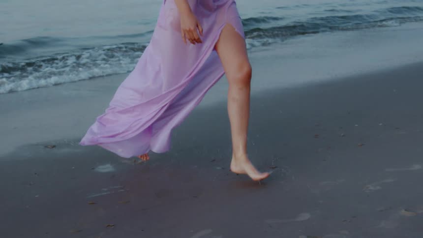 Woman in a flowing dress running barefoot along the beach shore