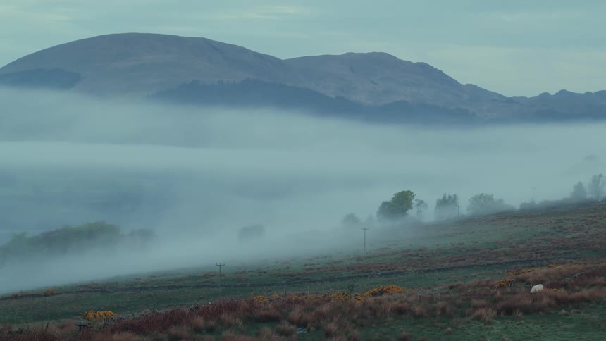 Fog covers a hilly plain with a mountain view in the background