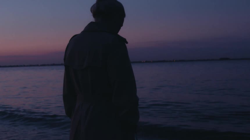 A woman deep in thought is standing with her feet in the ocean water