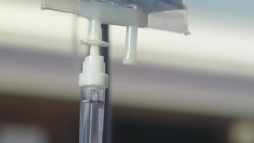 Close up of iv fluid dripping in a drip chamber connected to a medical iv fluid bag hanging on a pole