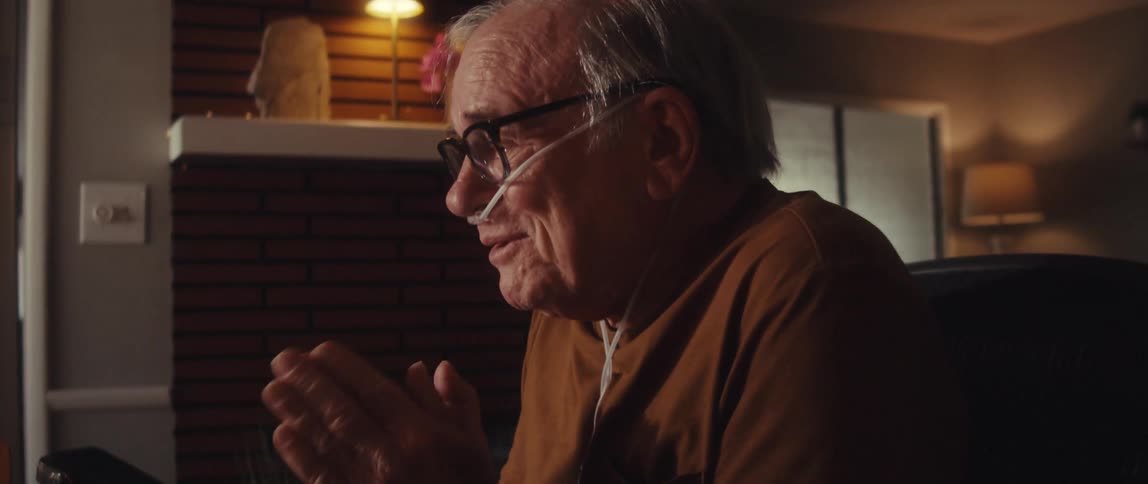 Elderly man sitting at a table with medical equipment talking happily