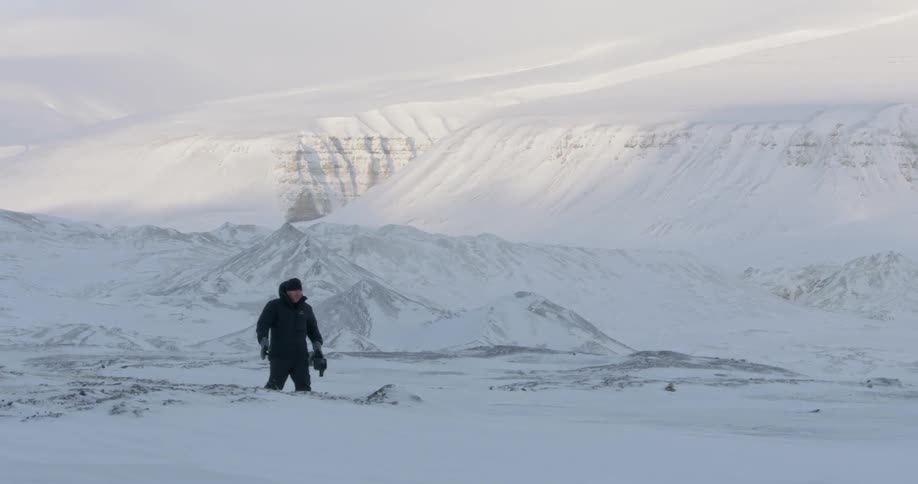A man is hiking along the snow carrying a large camera
