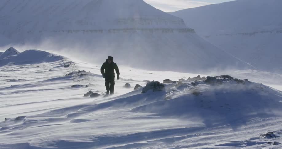 A man is hiking over rocks on a windy snowy day