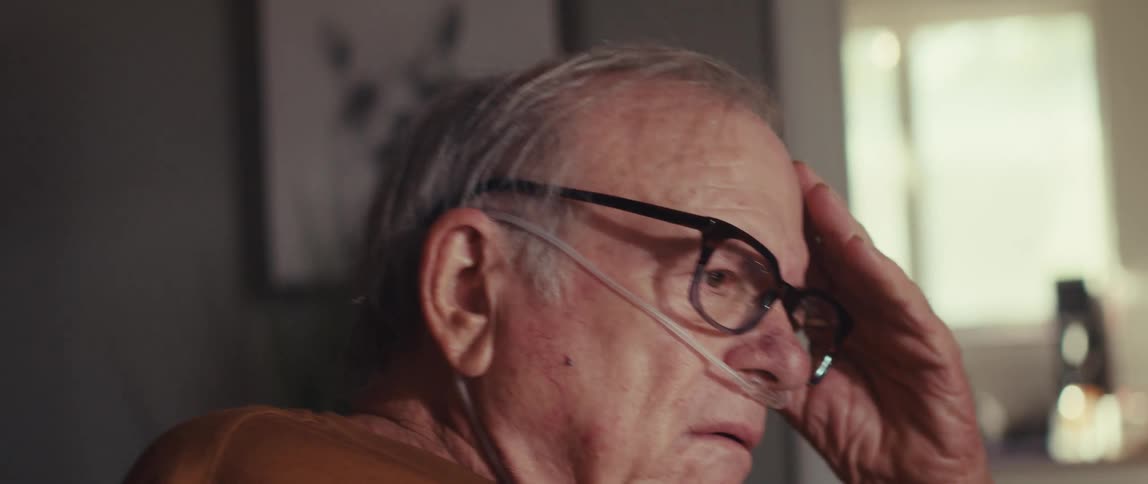 Elderly man sitting putting his hand on his face and getting scared