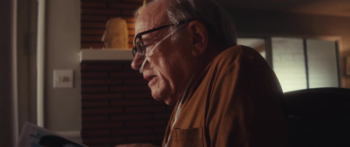 An elderly man has a video call with a doctor while sitting at his desk
