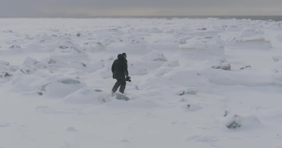 A man is hiking along the snow carrying a camera