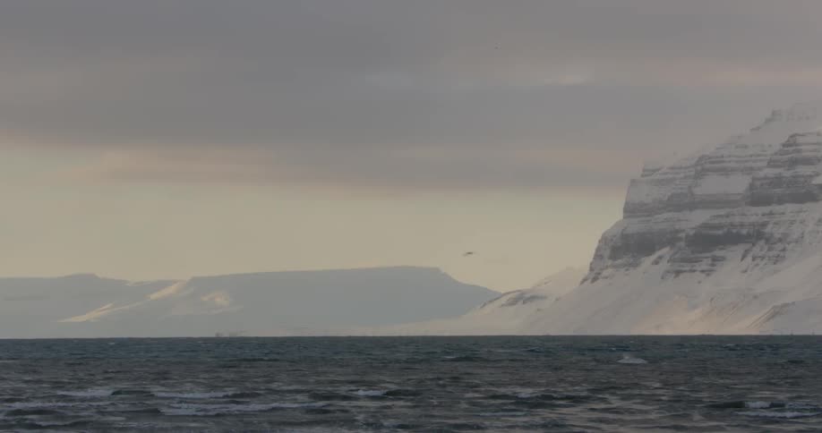 Dark clouds hang over the sea and snow-covered cliffs