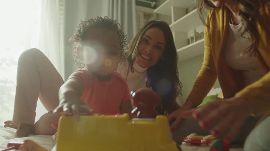 Grandmother shows baby parts of a toy while mother watches on
