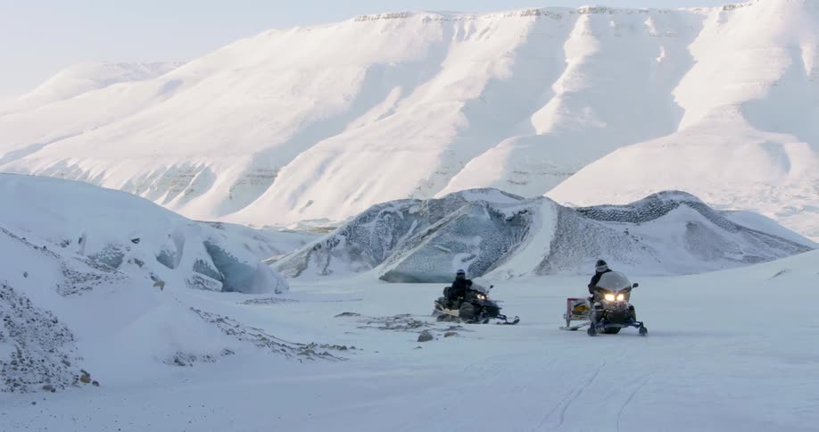 Two men a riding snowmobiles in a frozen landscape during the day