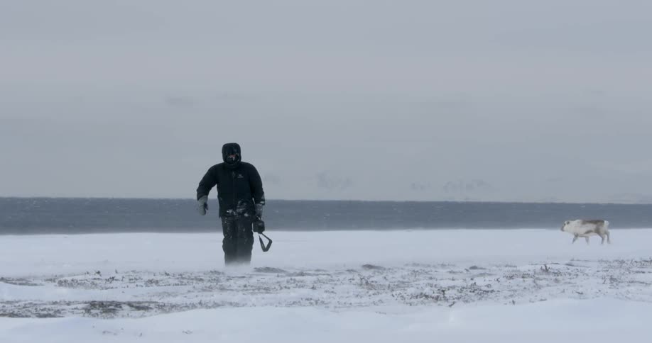 A man carrying a camera walks across a frozen landscape
