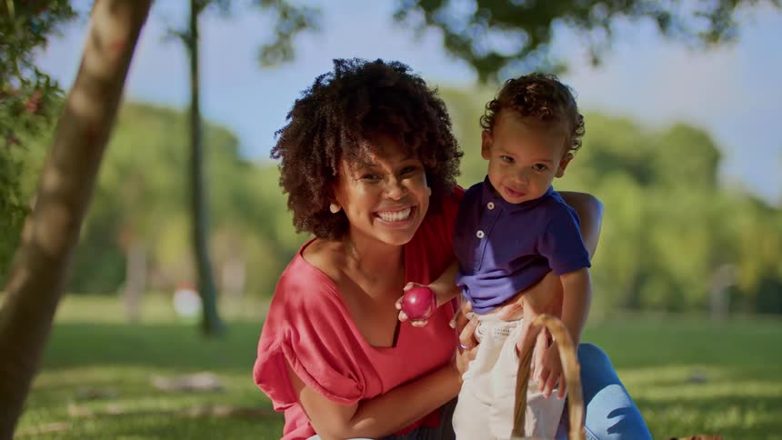 A smiling woman holds a toddler while enjoying a sunny day outdoors