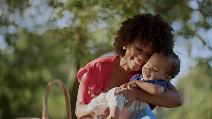 A smiling mother gently lifts her toddler in a sunlit park