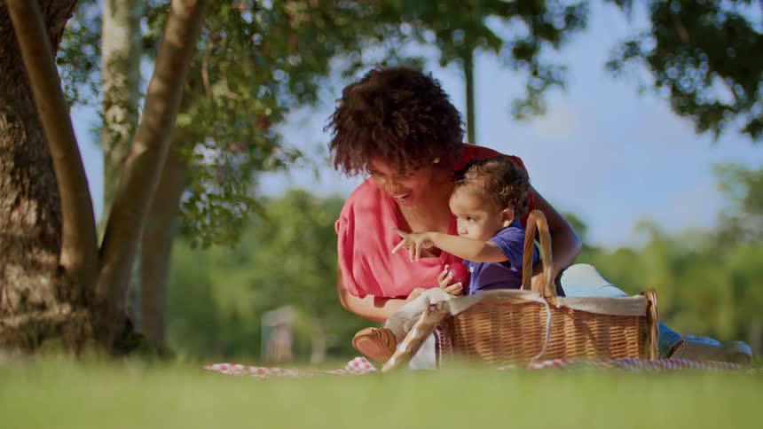 Woman and child sit on a picnic blanket pointing at something in the trees
