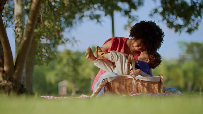 A joyful mother and child share a tender moment on a picnic blanket in a sunlit park