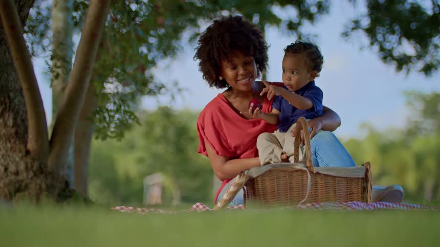 Mother and son sitting near a tree at midday pointing fingers