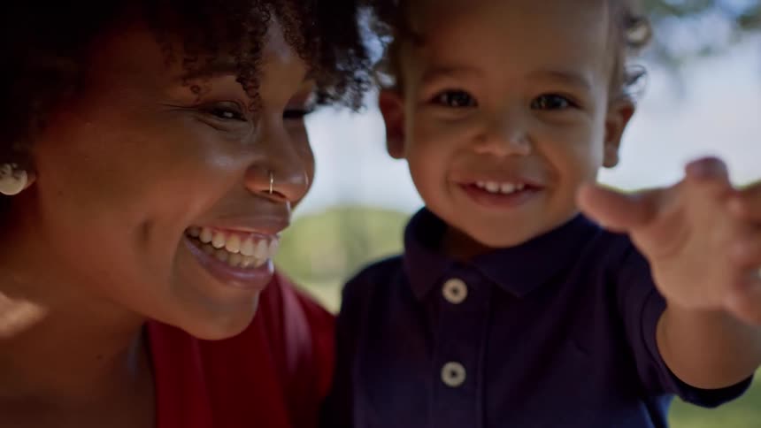 Portrait of a small boy together with his smiling mother in a grassy outdoor environment
