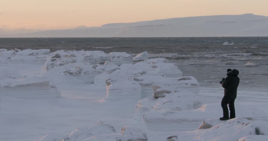 A man is photographing near the snow covered shore