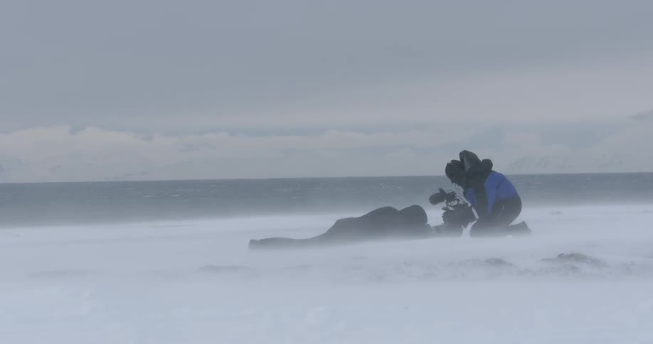 Two people taking pictures on a windy day in the snow