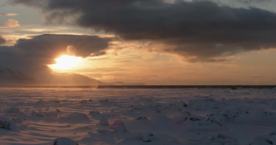 The sun shines behind clouds over a snowy landscape