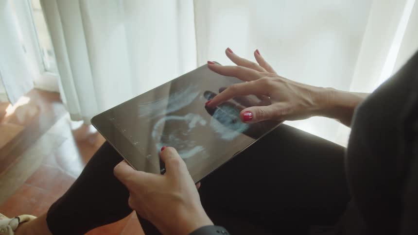 Woman hands interacting with a tablet displaying an ultrasound of a baby
