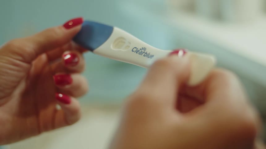 Close up of a woman holding a white and blue pregnancy test stick in her hands
