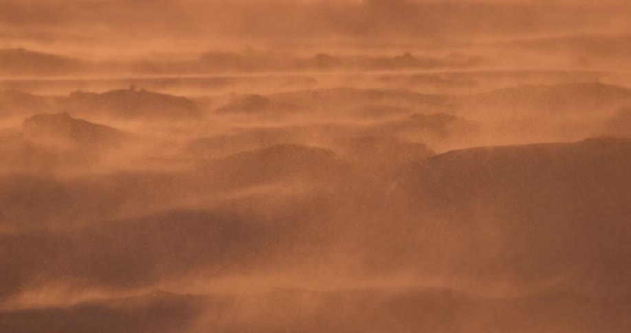 A red view of some hills with the wind blowing around dust or snow