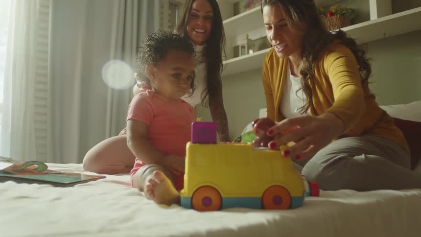 Two women with a child in a bed who is playing