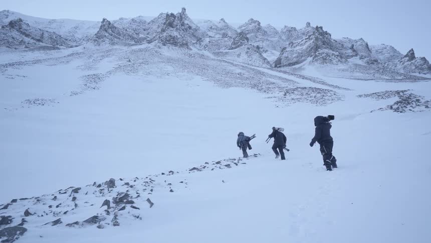 Three people carrying camera equipment hike over snowy terrain