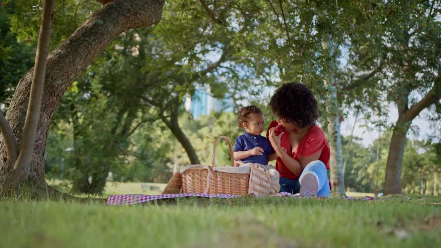 A mother and child enjoy a picnic together under a tree in a sunny park