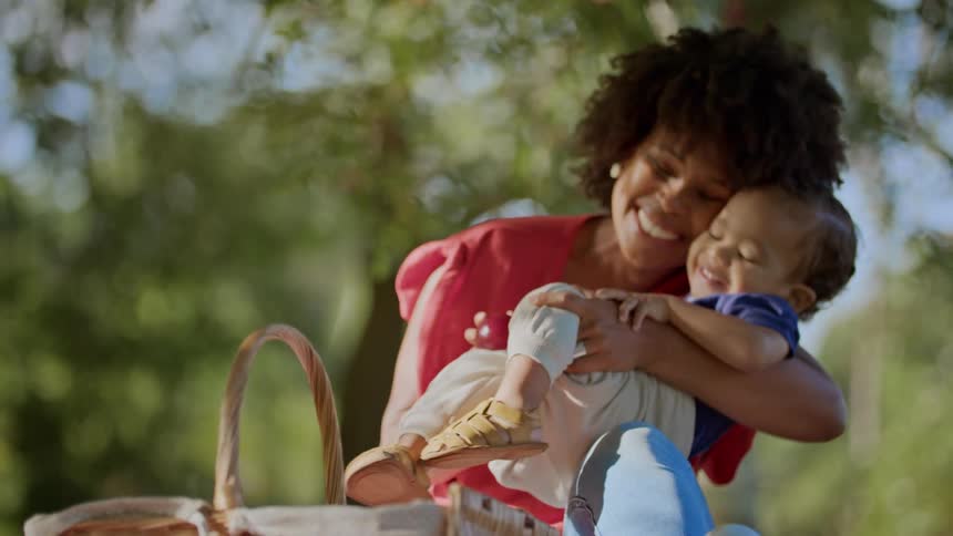 Mother hugs her toddler while they picnic in the park on a sunny day