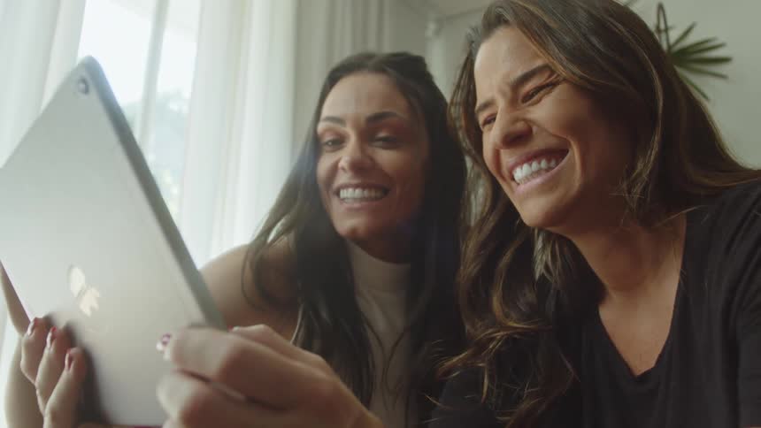 Two women laugh while looking at a tablet